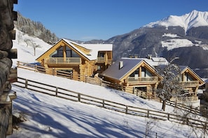 A wooden chalet with balconies, set against a snowy mountain backdrop.