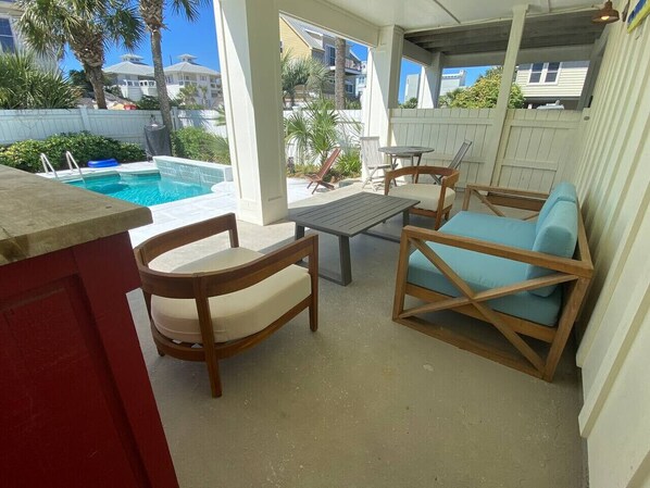 A covered outdoor area with a pool, wooden furniture, and a view of the surrounding neighborhood.