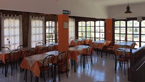 A dining area with tables and chairs, large windows, and a sign indicating the exit. - Casablanca (Villa Gesell)
