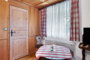 Een houten kamer met een geruit tafelkleed, een fles en glazen op een tafel, een radiator en een houten deur.