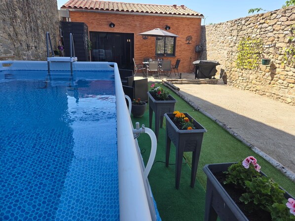 Una piscina con un motivo a rilievo esagonale, un muro in pietra e una zona patio con mobili da esterno e piante in vaso.