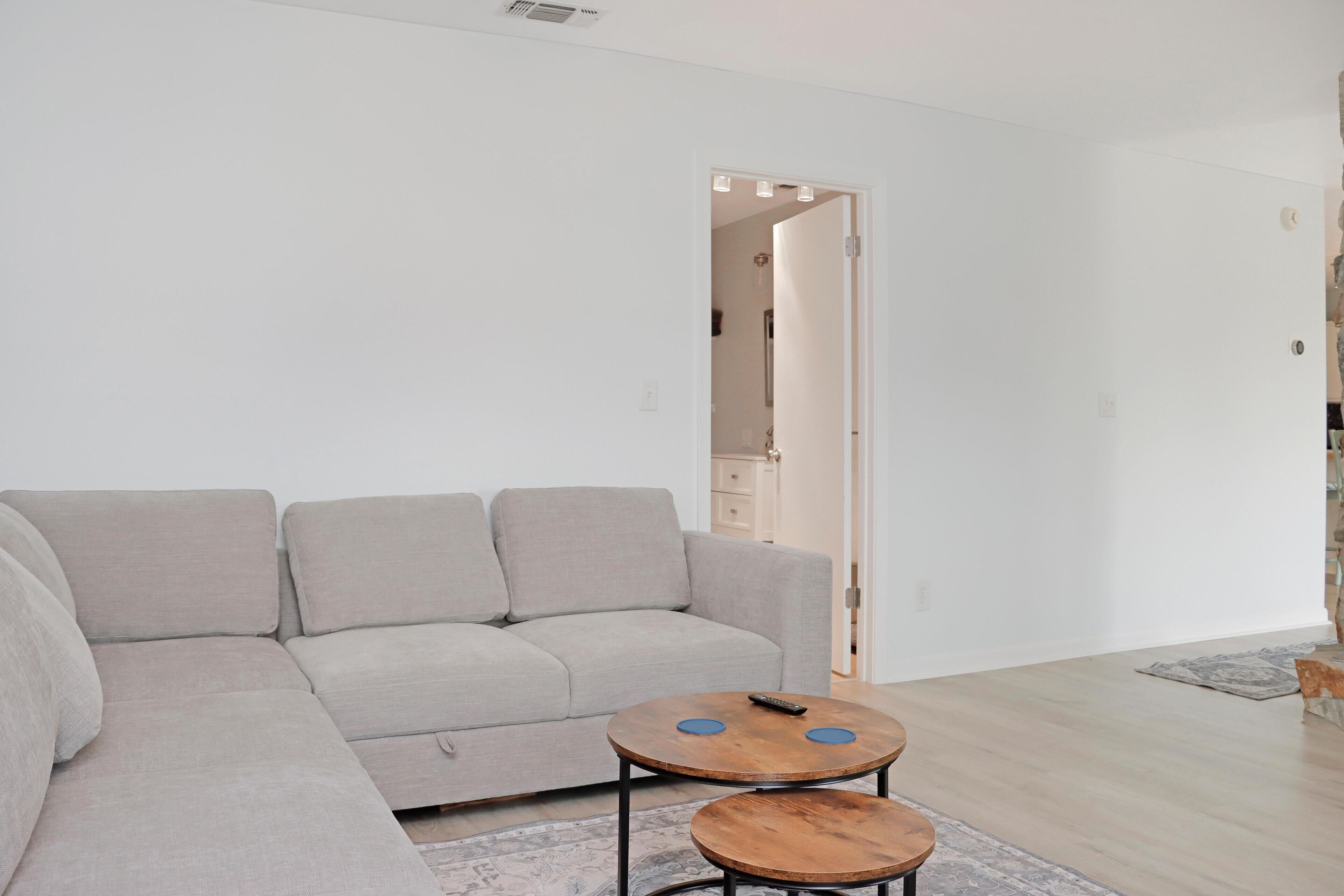 A modern living room with a grey sectional sofa, two wooden coffee tables, and a patterned rug.