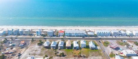 An aerial view of a coastal residential area with houses, a beach, and a road.