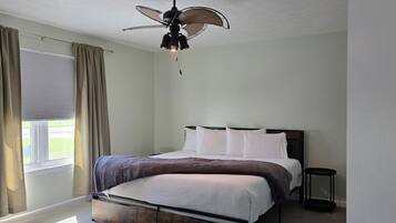 A bedroom with a bed, a ceiling fan, a window with curtains, and a bedside table.