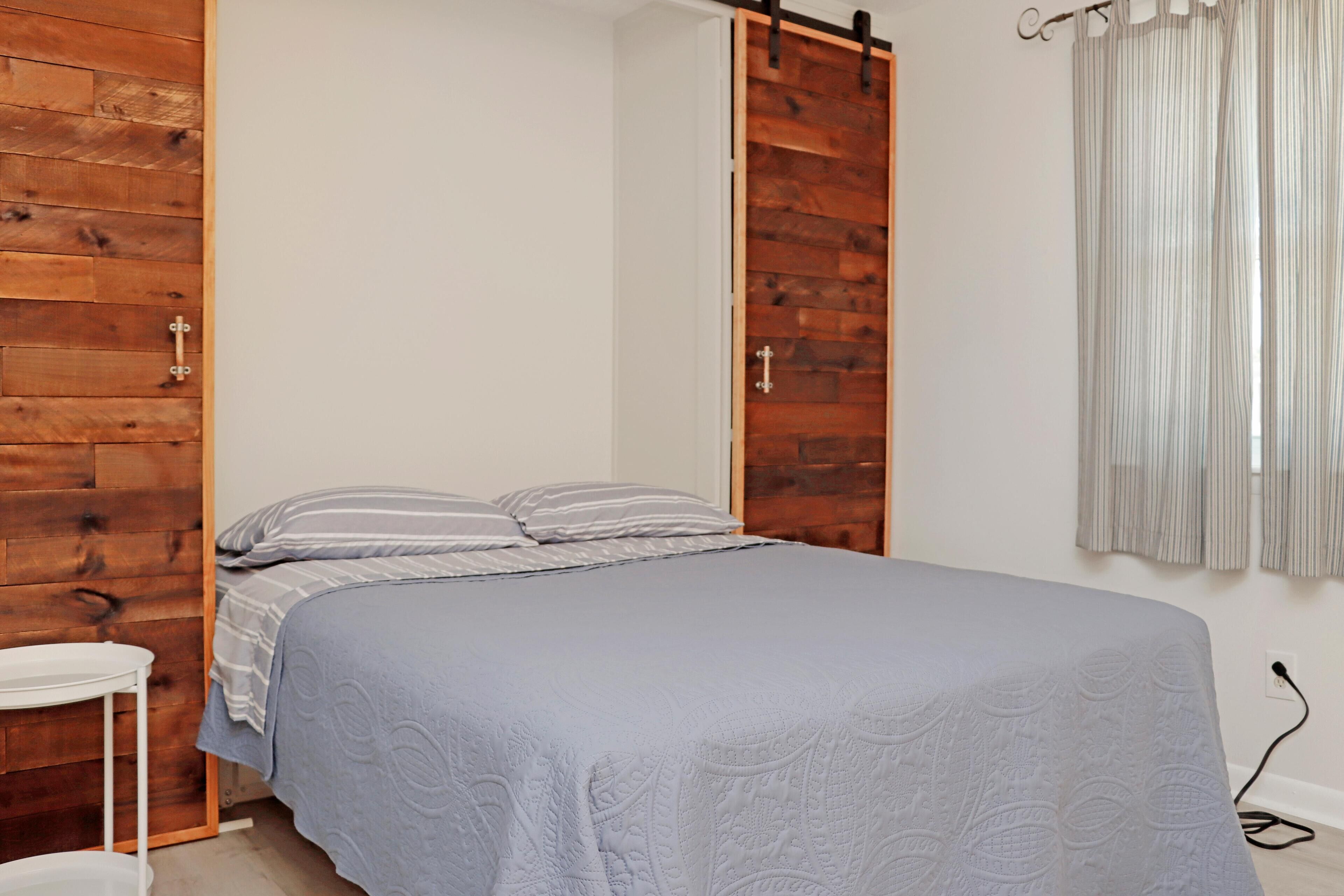 Ein Schlafzimmer mit einem Bett, einem Holzschrank, einem weißen Stuhl und einem Vorhang.