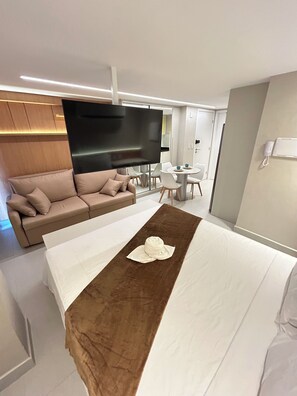 A modern hotel room with a large bed, a sofa, a dining table, and a TV.