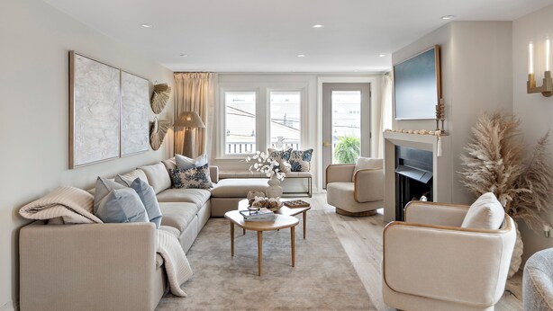 Een moderne woonkamer met een beige bank, een ronde salontafel en een open haard.