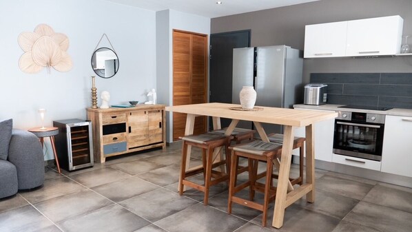 A modern kitchen with a wooden table and bar stools, a built-in oven, and white cabinetry.