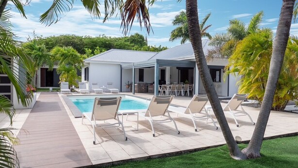 A modern pool area with lounge chairs, a covered patio, and a building with a white exterior. - Villa La Rosière, luxury 4-suite villa, private pool & jacuzzi (STE ANNE)