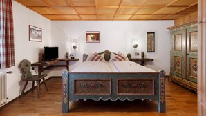 A bedroom with a wooden ceiling, a bed with floral designs, a desk with a computer, and a cabinet with decorative panels. - Standard Double Room with Shared Garden, Balcony and Wi-Fi (Schramberg)