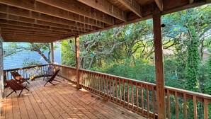 A wooden deck with a railing, two lounge chairs, and a view of trees and a house in the background. - Amazing ocean views, Sleeps 8, Beach access, Pets OK (Surf City)