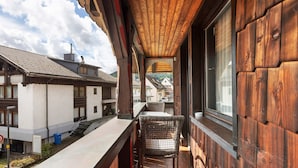 A balcony with a wooden ceiling, a wicker chair, and a view of neighboring buildings. - Large Double Room with Shared Garden, Balcony and Wi-Fi (Schramberg)