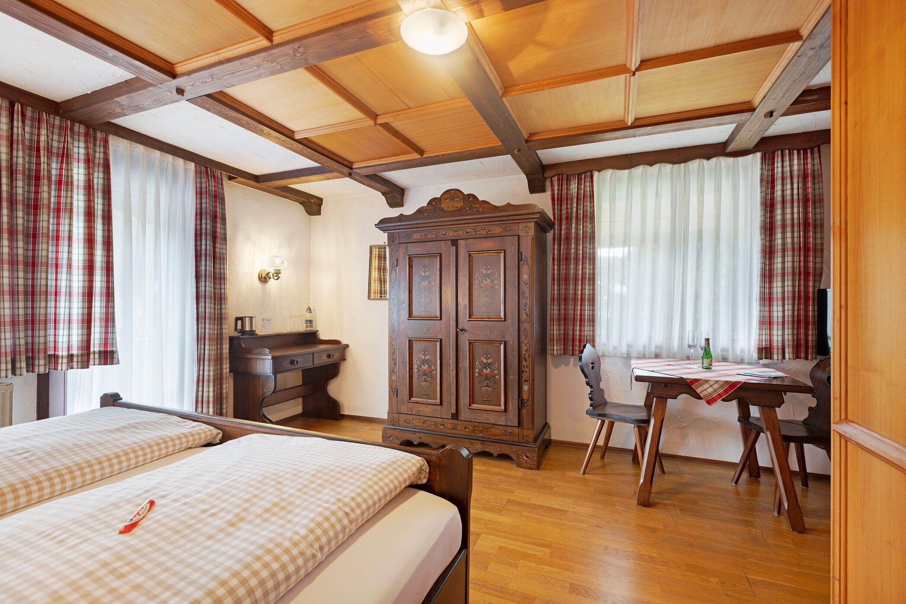 Una habitación con dos camas, un armario de madera, una mesa con sillas y una ventana con cortinas.