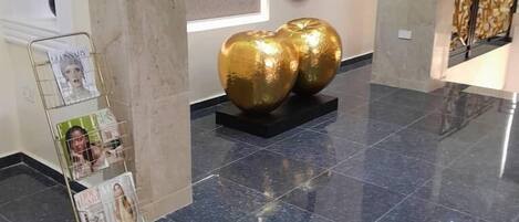En entréhall med ett marmorgolv, ett tidningsställ och två gyllene, sfäriska skulpturer.