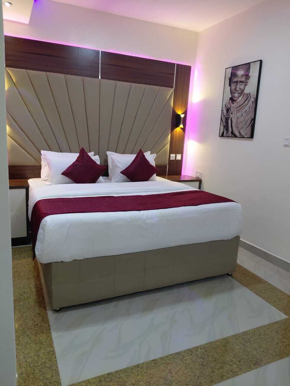 A hotel room with a bed, a headboard, a nightstand, and a wall-mounted picture.