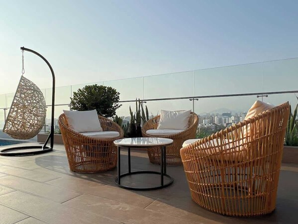 Eine Dachterrasse mit Korbmöbeln, einem Hängesessel und Blick auf die Stadt.