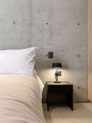 Ein Schlafzimmer mit einem Bett, einem Nachttisch, einer Lampe und einer Wand mit einem Lichtschalter.