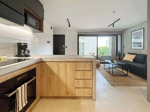 A modern kitchen with a wooden island, a dining area with a sofa and coffee table, and a large sliding glass door leading to a balcony.
