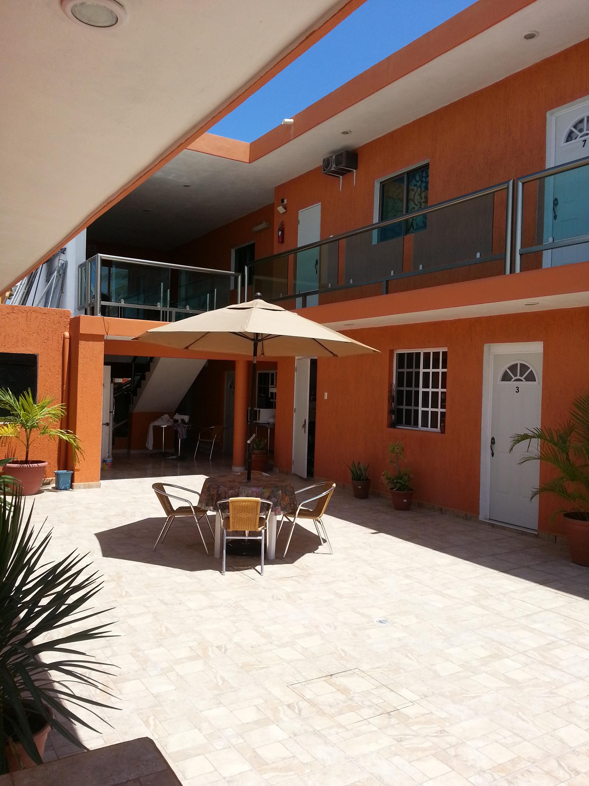 Un patio techado al aire libre con una mesa y sillas, plantas en macetas y una barandilla de cristal que da a un nivel inferior.