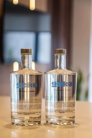 Kaksi Geko-alkoholipulloa heijastavalla pinnalla, taustalla epätarkka kuva.