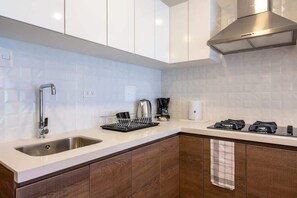 A modern kitchen with a stainless steel sink, a coffee maker, and a range hood. - geko| Cramme_ 1BR close by MAC museum in Barranco (Lima)