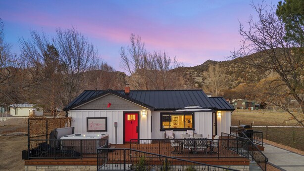 A house with a red door, a patio with outdoor furniture, and a small garden with a decorative rooster. - 1900's Farmhouse (New Castle)