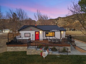 Une maison avec une porte rouge, une terrasse avec des meubles d’extérieur et un petit jardin agrémenté d’un coq décoratif.