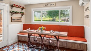 A dining area with a bench, a table with plates and a vase of flowers, and a window with a view of a green landscape. - 1900's Farmhouse (New Castle)