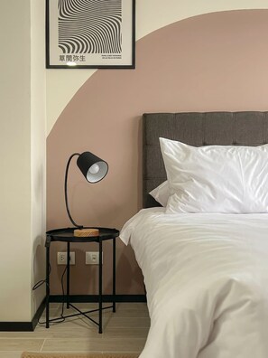 Un dormitorio ordenado con cama, una mesita de noche con lámpara y una obra enmarcada en la pared.