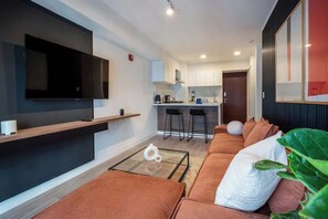 A modern living room with a flat-screen TV, a sofa, a coffee table, and a kitchen area in the background. - Geko | Comfortable 1BR w/ Pool near Barranco (Lima)
