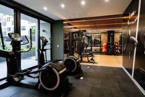A gym with exercise equipment, large windows, and a view of buildings outside. - Geko | Comfortable 1BR w/ Pool near Barranco (Lima)