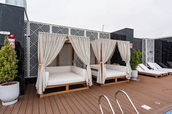 Deux lits à baldaquin blancs, dotés de rideaux, une terrasse en bois et des chaises longues.