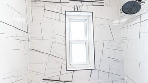 Ein Badezimmer mit weiß gefliester Wand, abstrakten schwarzen Linien, einem Fenster und einer Duschbrause.