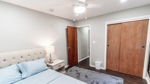 Ein Schlafzimmer mit einem Bett, einem Nachttisch, einer Lampe, einem Holzschrank und einem Deckenventilator.