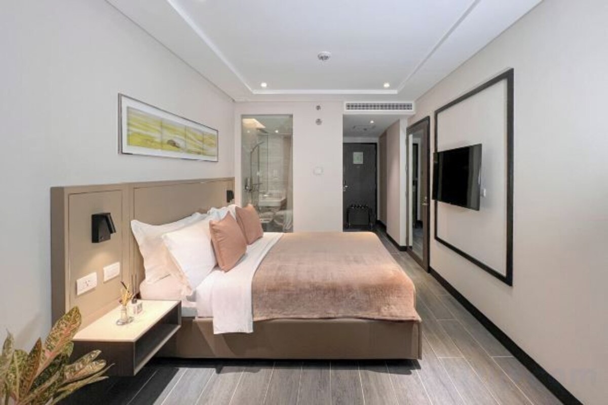 A modern hotel room with a large bed, bedside tables, a flat-screen TV, and a framed picture on the wall.