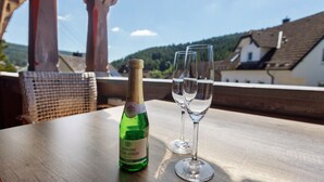 Une bouteille de vin Schlosser Königstein et deux verres sur une table, avec vue sur des bâtiments et des collines.