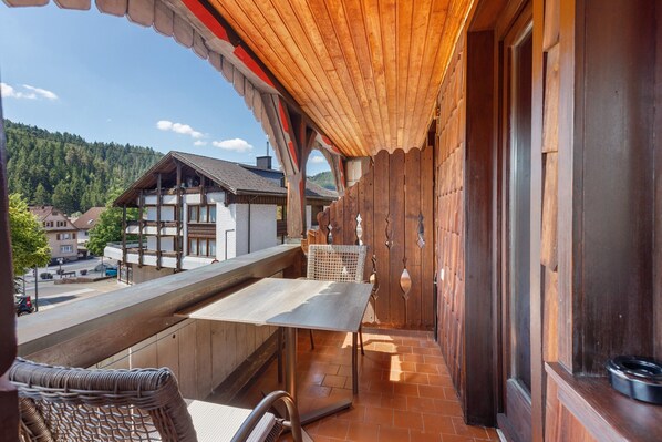 A wooden balcony with a table and chairs, a view of a town, and a mountain in the background.