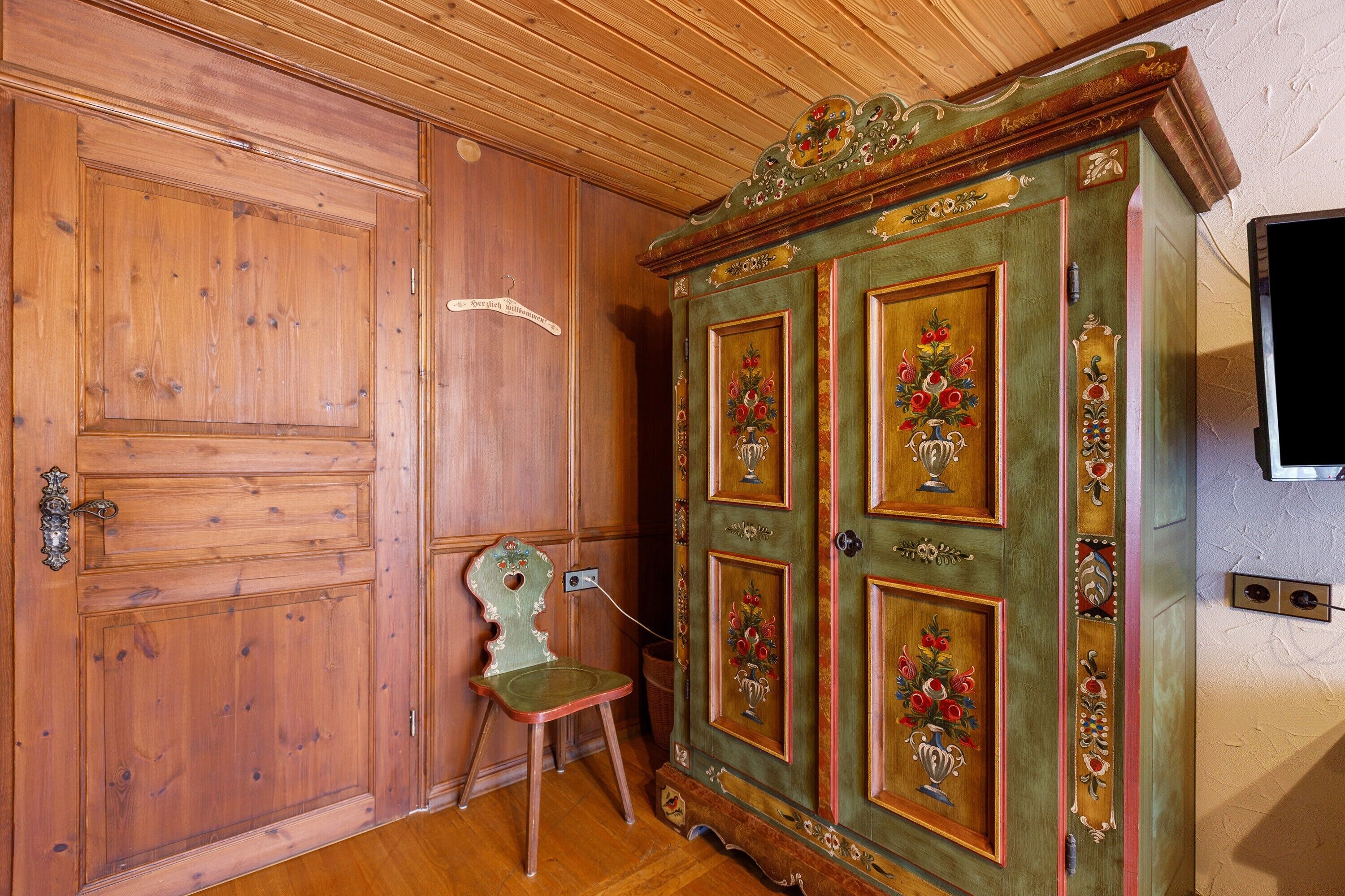 Een houten deur, een groene kast met bloemmotieven, en een stoel.