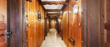A wooden hallway with a tiled floor, wooden doors, and a ceiling with exposed beams.