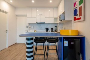 A modern kitchen with white cabinets, a marble countertop, a black refrigerator, and two black bar stools. - Geko l Contemporary 1BR in Barranco w/ balcony (Lima)