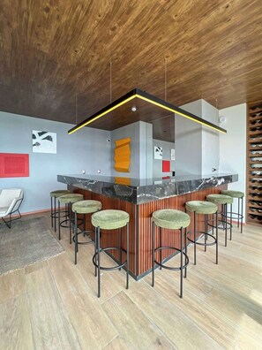 A modern bar area with a wooden ceiling, a marble countertop, and green upholstered stools.