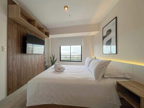 Une chambre d’hôtel moderne dotée d’un grand lit, d’une télévision, d’une fenêtre donnant sur la ville et d’une tête de lit en bois.
