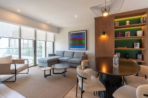 A modern living room with a sectional sofa, a round dining table, and a bookshelf. - Geko | Panoramic 2BR w/ Ocean view in Barranco (Barranco)