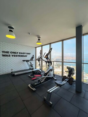 A gym with treadmills, elliptical machines, and a rowing machine, large windows with a city view, and a motivational quote on the wall. - Geko | Panoramic 2BR w/ Ocean view in Barranco (Barranco)