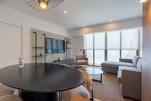 A modern living room with a round table, a sofa, a TV mounted on the wall, and large windows. - Geko | Panoramic 2BR w/ Ocean view in Barranco (Barranco)
