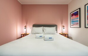 A neatly made bed with white linens and pillows, two bedside tables with lamps, and framed artwork on the wall.
