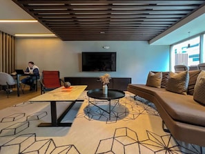 Ein moderner Lounge-Bereich mit einer Couch, einem Couchtisch und einem an der Wand montierten Fernseher.