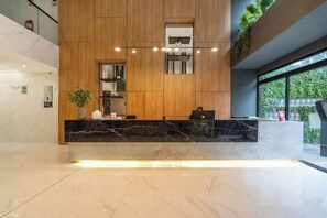 A reception area with a marble counter, wooden paneling, a small plant, and a window with a view of greenery.