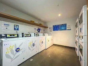 Un cuarto de lavandería con varias lavadoras, un panel de control digital y carteles informativos en la pared.