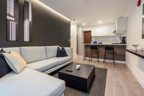 A modern living room with a sofa, a coffee table, and a kitchen area with bar stools.